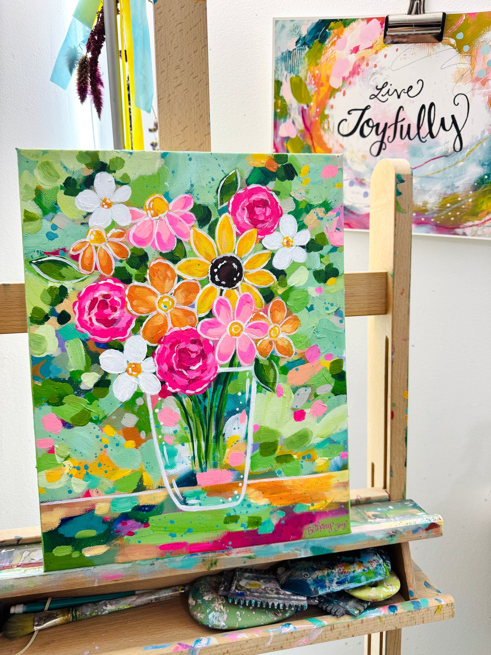 Colorful floral painting on an easel with art supplies underneath