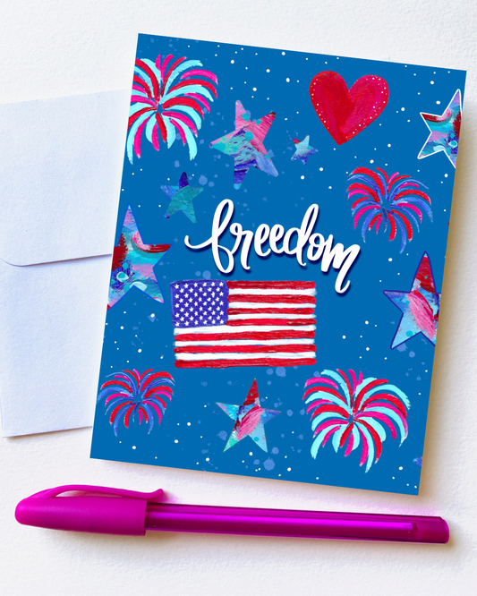 Greeting card with American flag, heart, and fireworks on a blue background, accompanied by a pink pen.