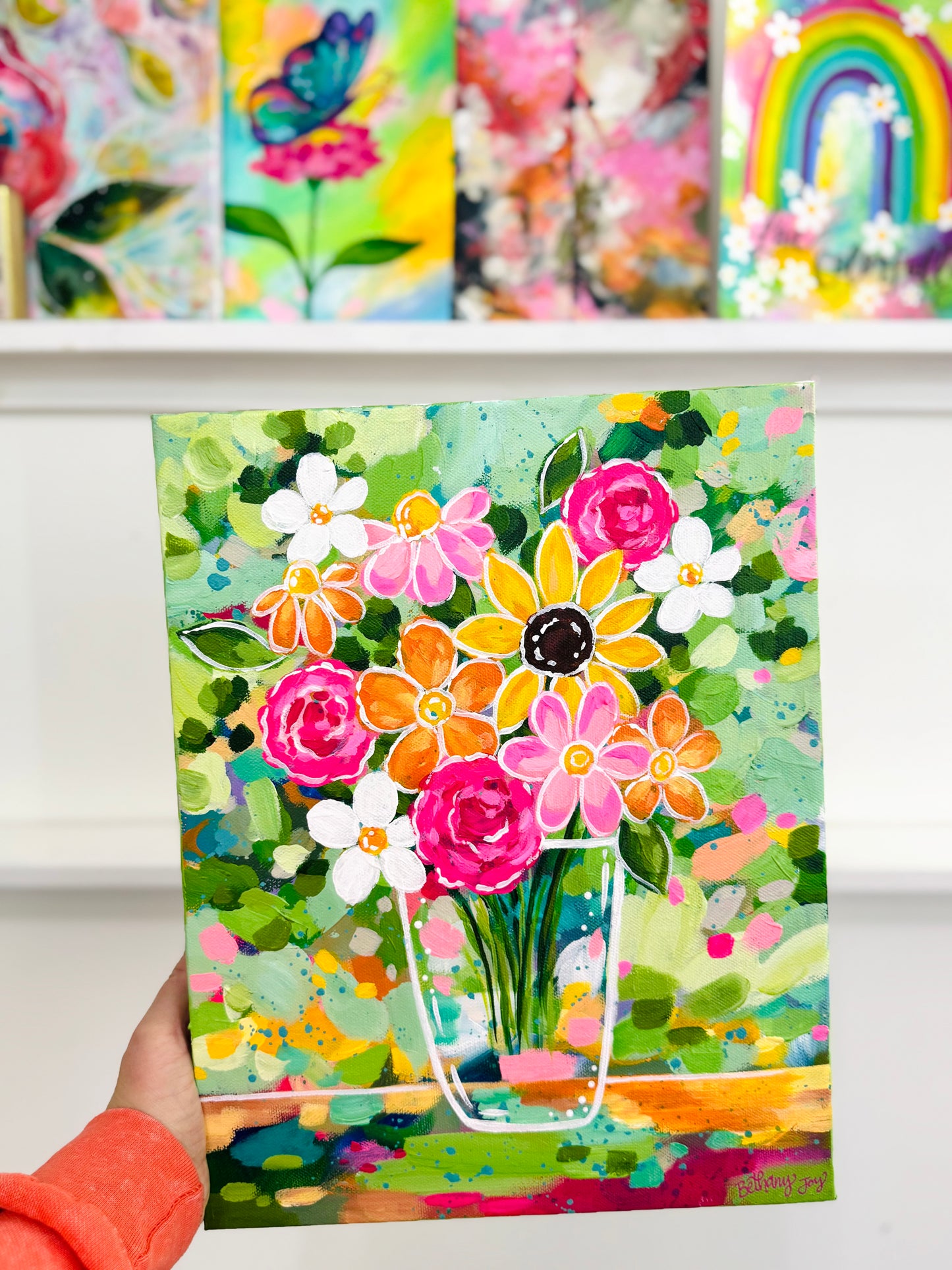 Colorful painting of flowers held by a person with more artwork in the background