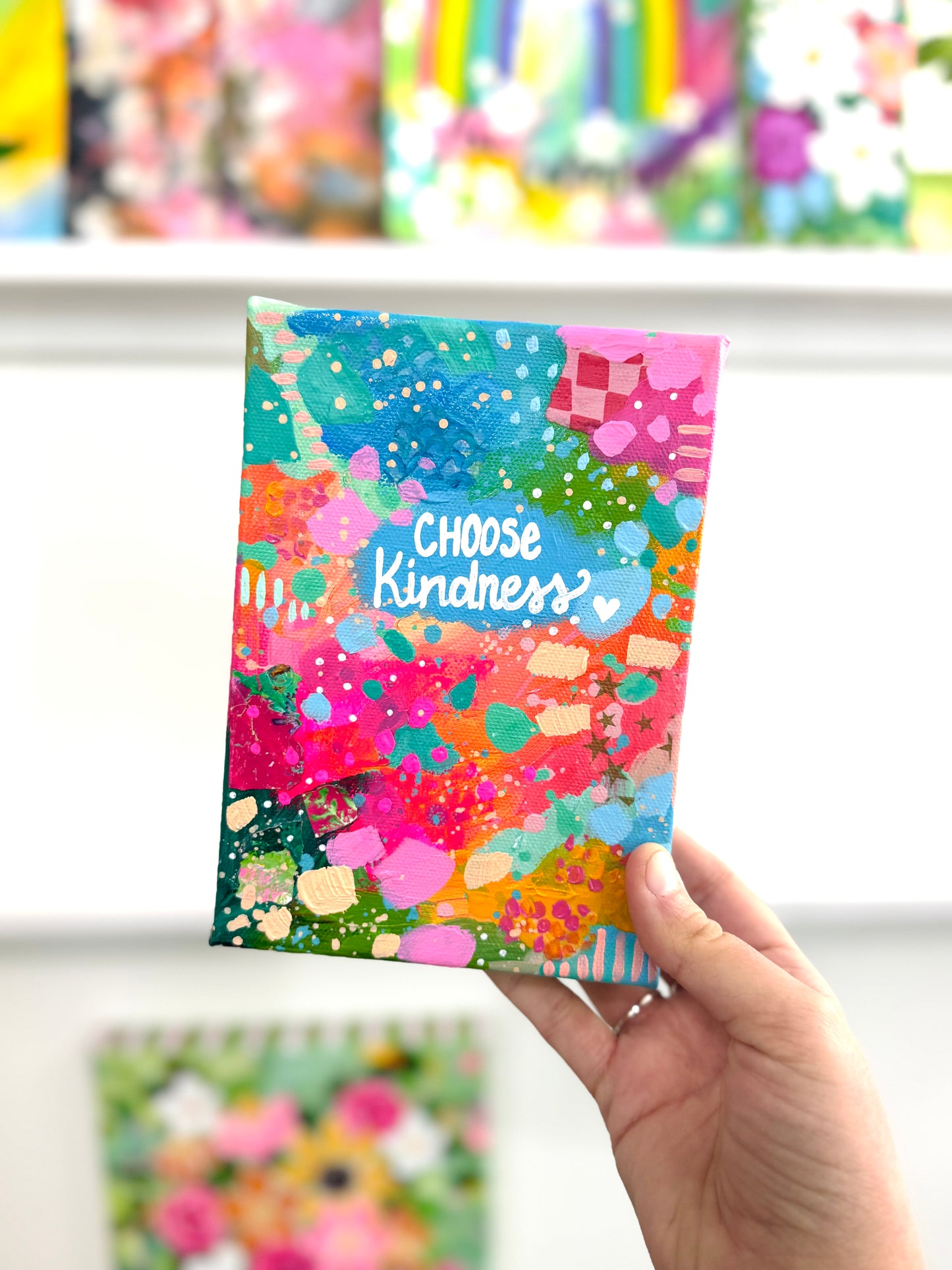 Abstract colorful canvas with the words choose kindness painted on with more art blurred in the background 